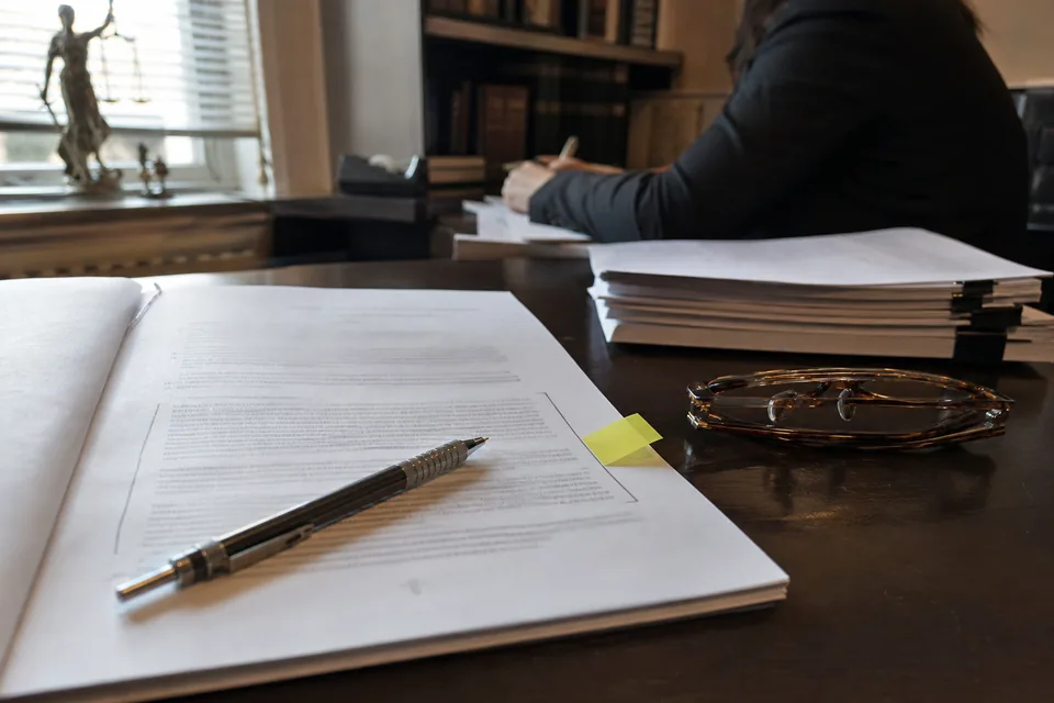 Printed mutual non-disclosure agreement with pencil brackets around one clause and a yellow tab, on a desk next to reading glasses
