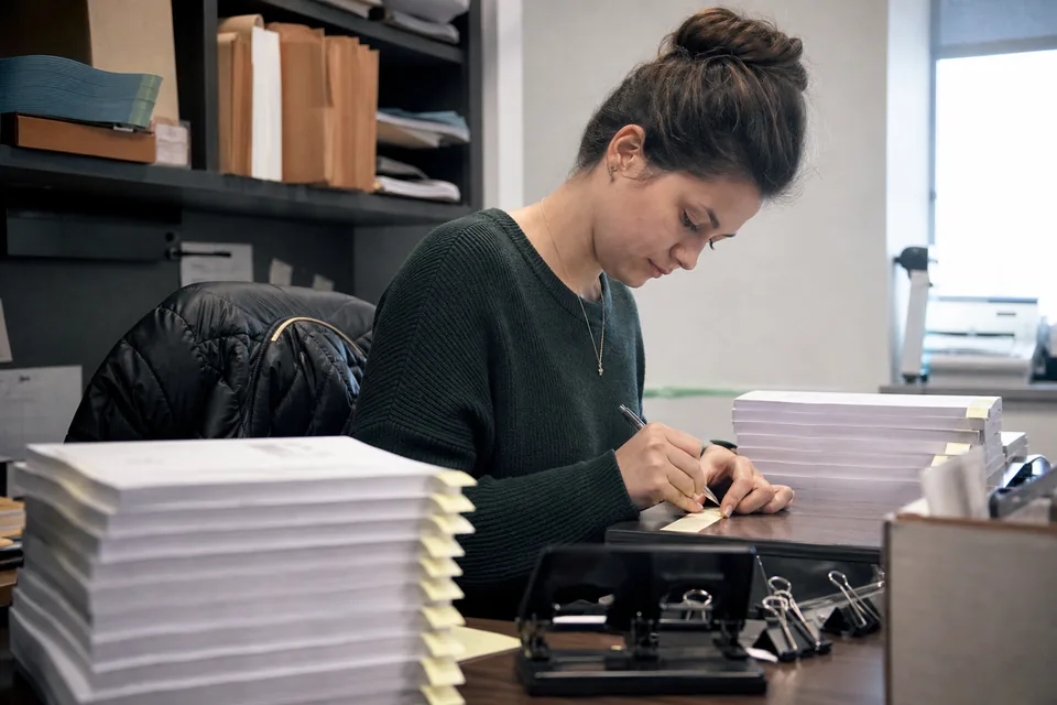 Paralegal labeling exhibit tabs at a workstation stacked with exhibits