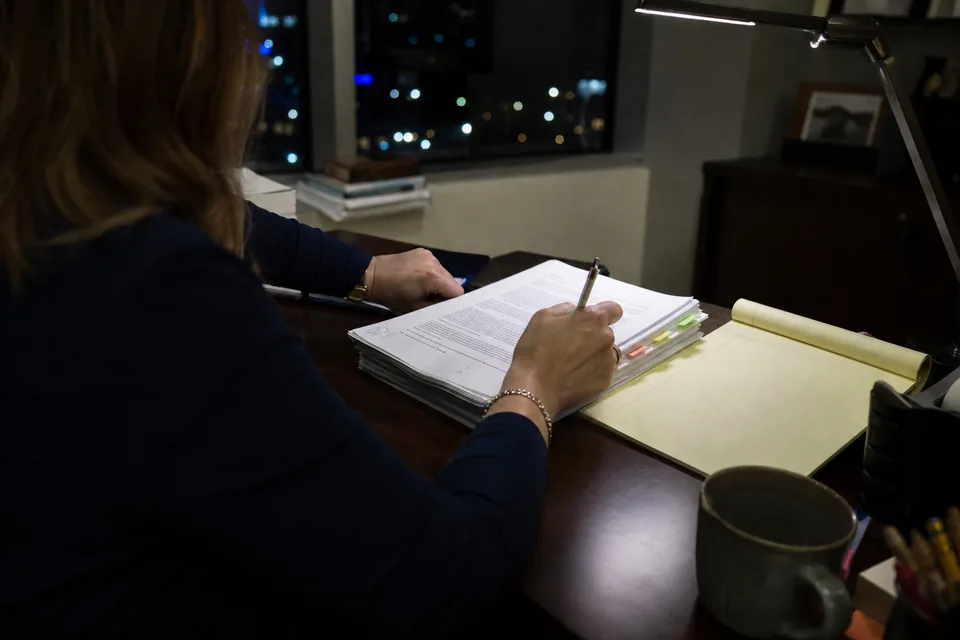 Attorney's hands with a pencil over a printed contract with colored page tabs on a law office desk in the evening