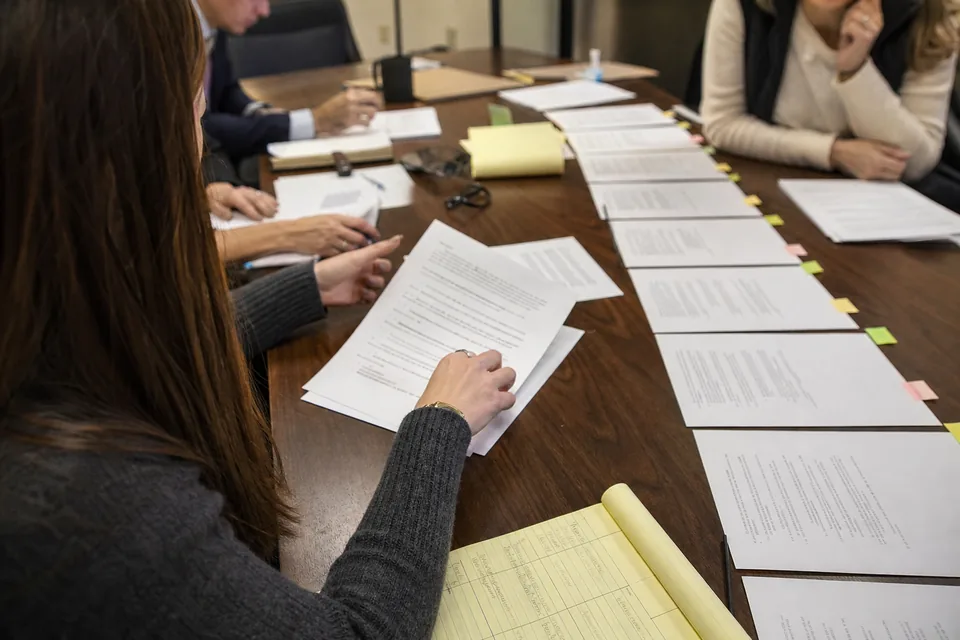 Hands arranging printed emails and deposition pages in date order on a table