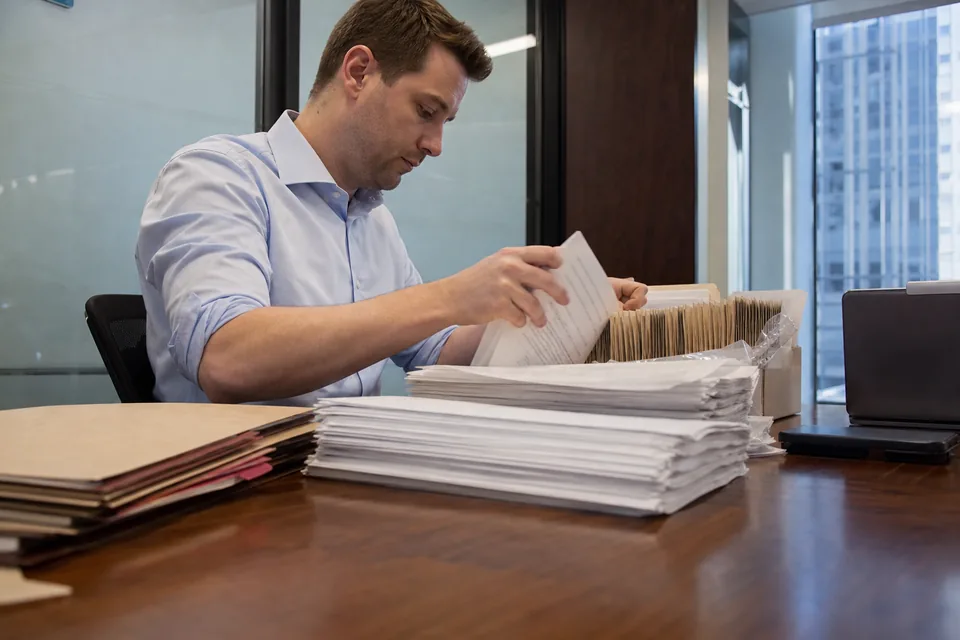 Paralegal sorting a stack of produced documents into folders on a conference table